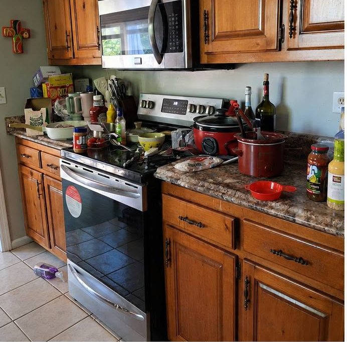 A kitchen counter and stove covered in clutter and spills before cleaning